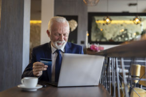 Senior businessman sitting at a restaurant table, purchasing over the internet and paying with a credit card