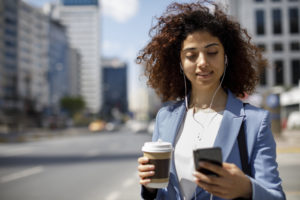 A young businesswoman looks at her phone in one hand and holds a cup of coffee in the other