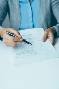 A business person in a blue collared shirt extends a pen towards the recipient