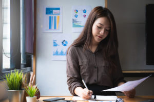 A young woman stands at a table and makes financial calculations