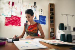 Feature image of a young woman of color typing on a calculator while looking at financial documents