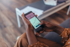 Feature image close-up of a woman of color holding a smartphone that displays a graph of market trends