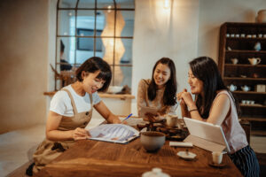 Featured image of three Asian women sitting around a table while looking at a tablet