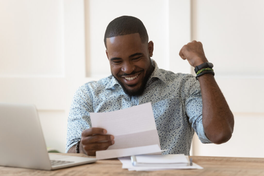 Featured image of a young Black man smiling while reading a piece of paper