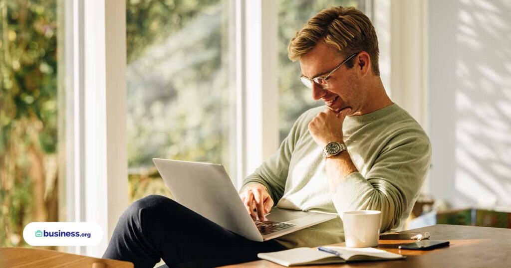 male using computer in bright room with foliage outside of window